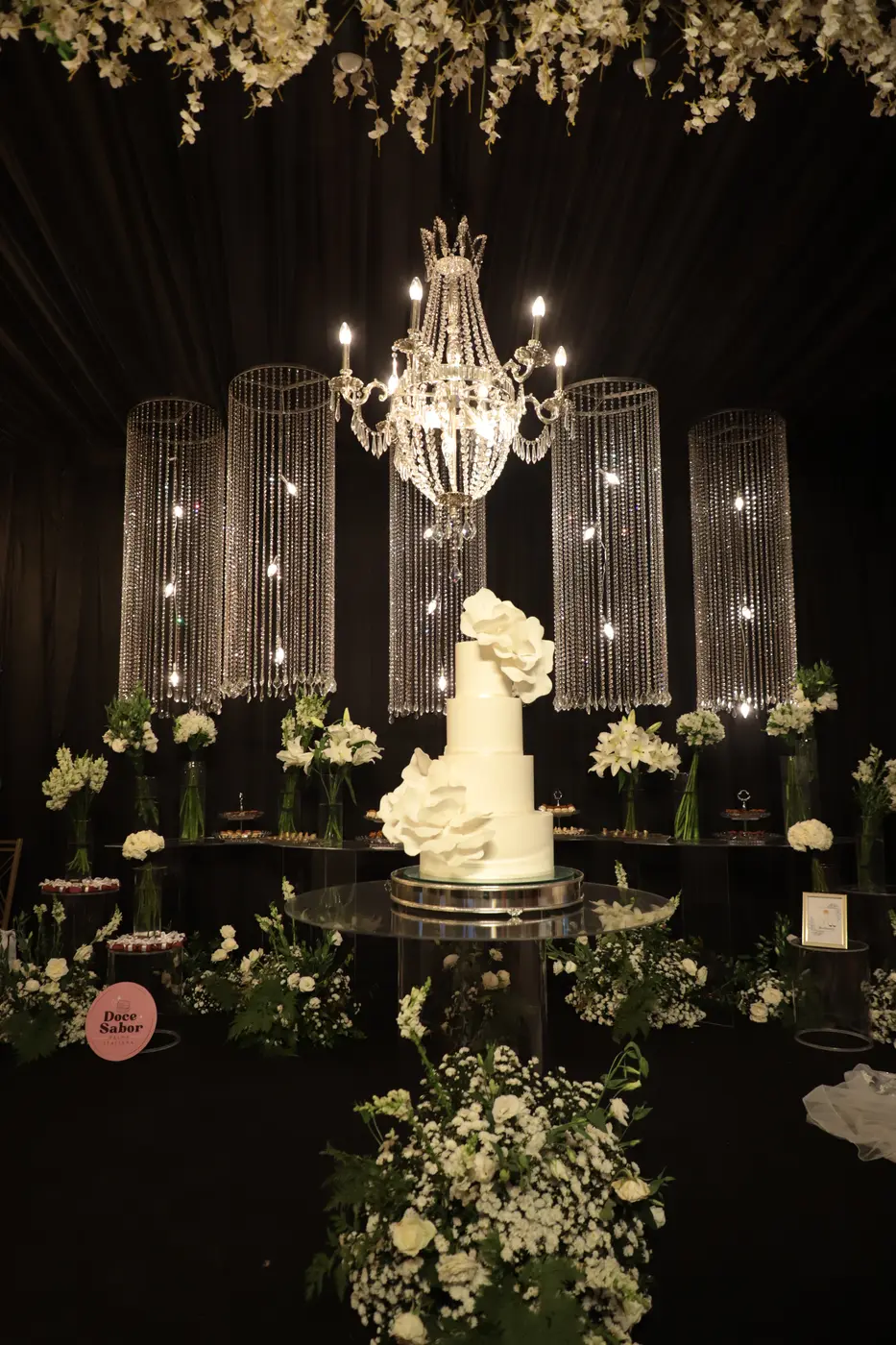 Mesa de doces da 1ª Expo: bolo branco com flores, lustre e cortinas de cristal