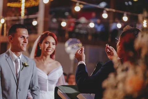Noivos sorrindo durante a festa, varal de luzes ao fundo