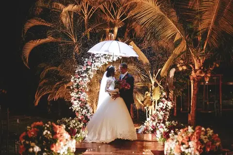 Casal de noivos sob sombrinha branca em noite de chuva