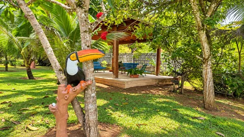 Quiosque de madeira com bancos no jardim, tucano decorativo em primeiro plano