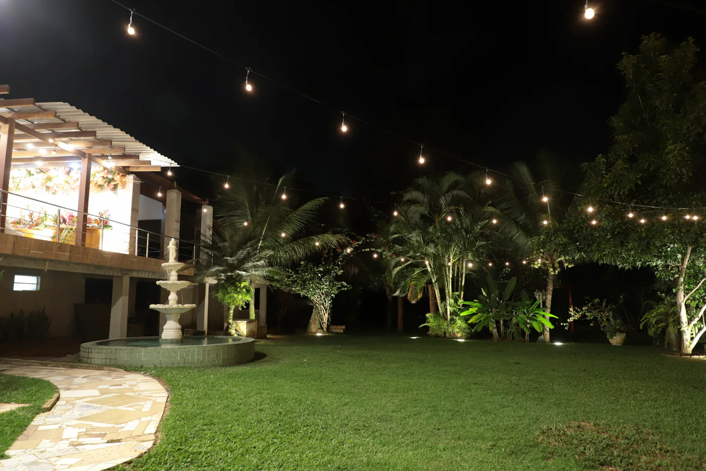 Jardim da chácara ao anoitecer, com chafariz e varal de luzes