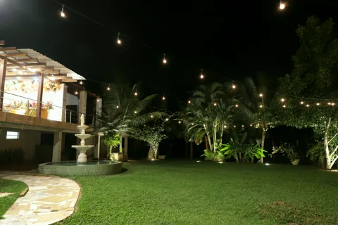 Jardim iluminado à noite com chafariz e varal de luzes