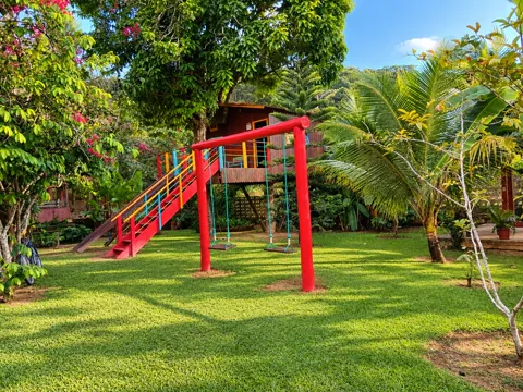 Balanço vermelho no gramado com a casinha na árvore ao fundo