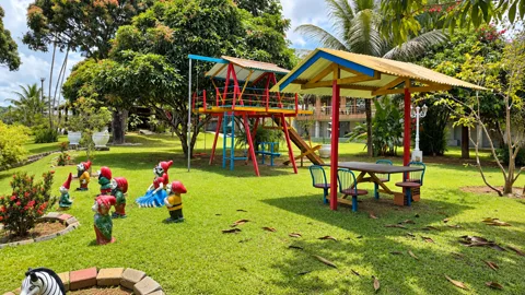 Parquinho com torre, escorregador e mesinha coberta no gramado, cercado de anõezinhos decorativos